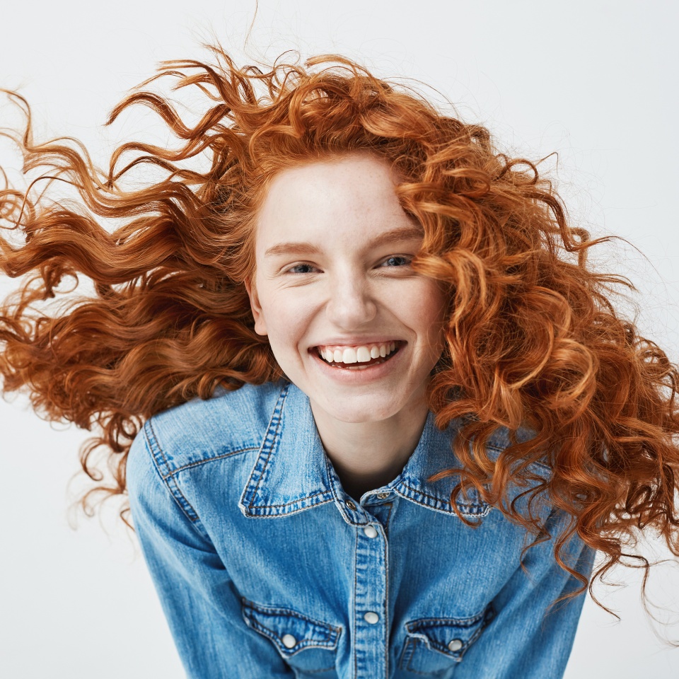 Portrait of beautiful happy cheerful redhead girl with flyingcurly hair smiling laughing looking at camera over white background.