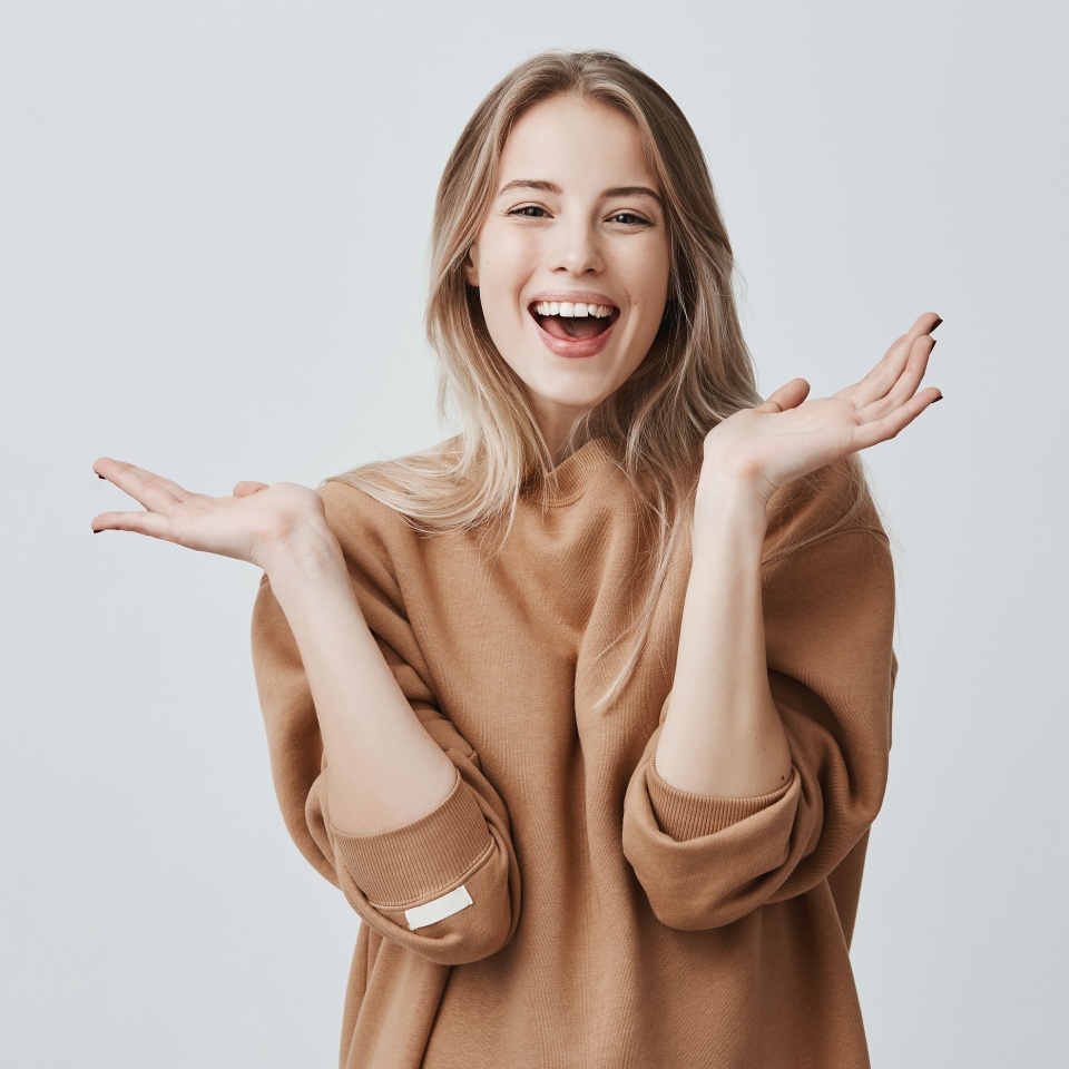 Pretty beautiful woman with blonde long hair looking at camera having excited and happy facial expression, clapping with her hands against blank studio wall, expressing her excitement with present