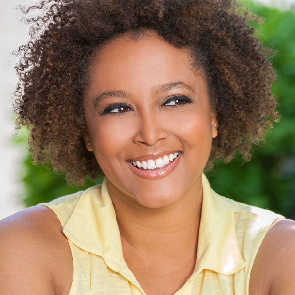 Beautiful young mixed race black African American woman with perfect teeth smiling and relaxing outside in summer sunshine