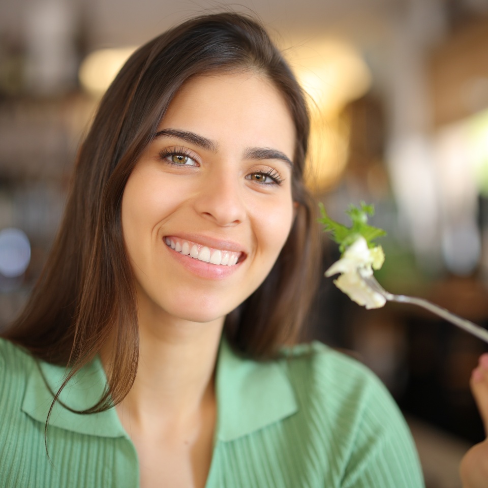 Happy woman holding fork with lettuce in a restaurant looking at camera