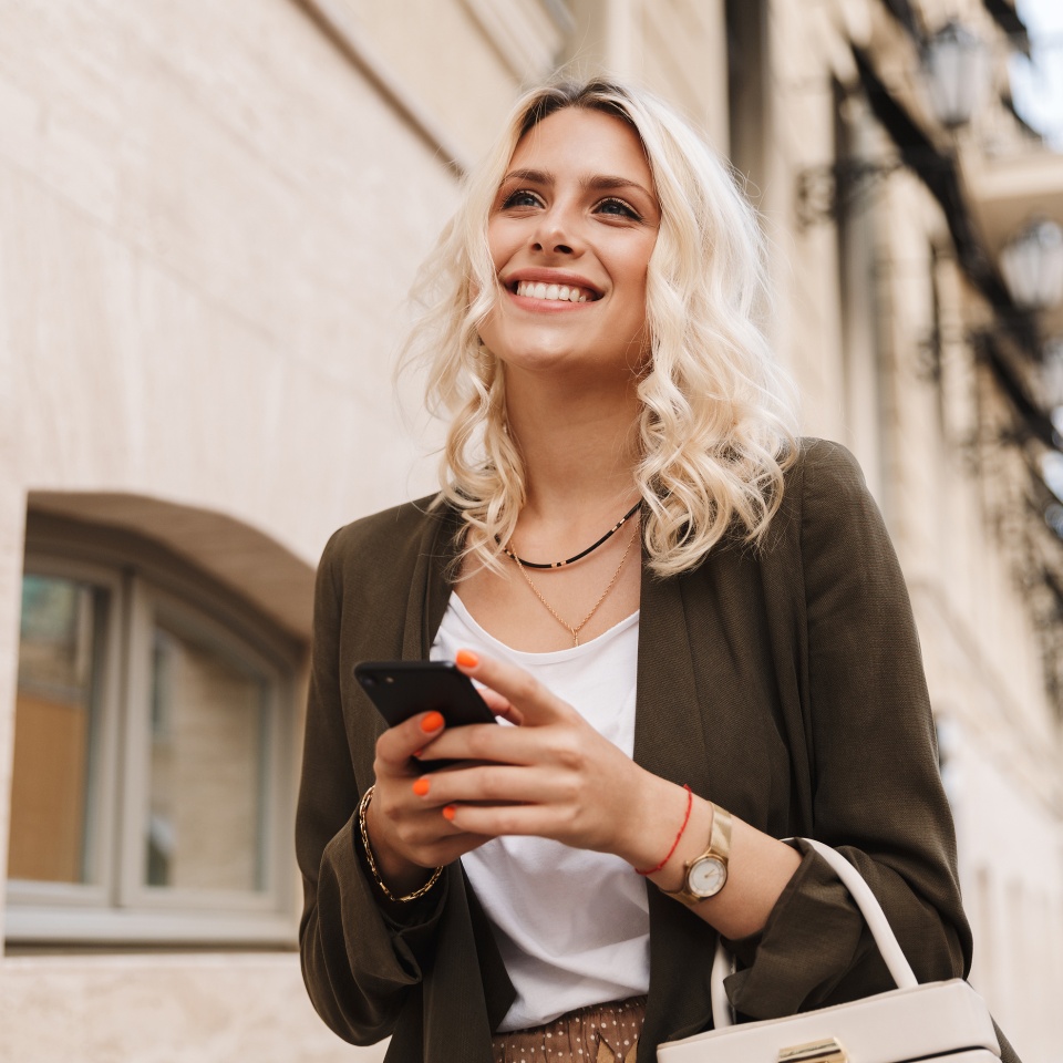 Image of caucasian woman wearing jacket using mobile phone for chat while walking through city street