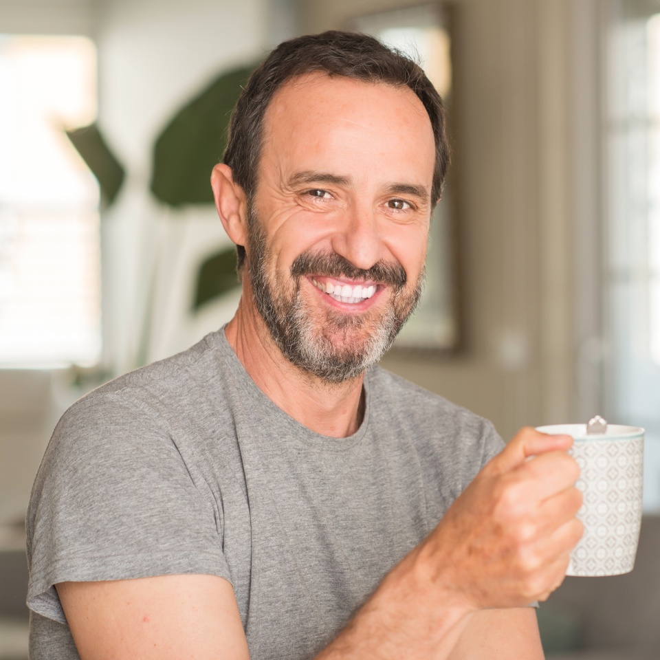 Middle age man drinking coffee in a cup with a happy face standing and smiling with a confident smile showing teeth