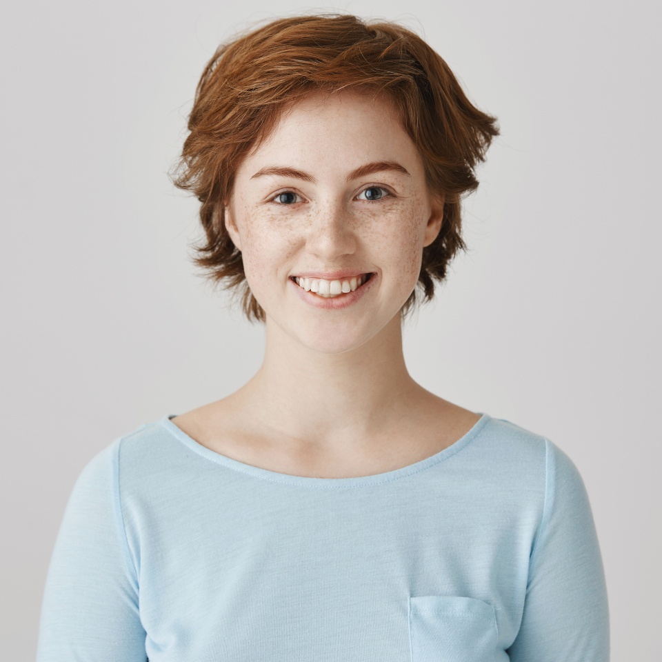 Nice to meet you. Portrait of friendly good-looking female student with short ginger hair smiling broadly and expressing positive attitude over gray background. Sister likes cooking together with mom
