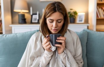 Sickness, seasonal virus problem concept. Woman being sick having flu drinking tea on sofa. Sick woman lying in bed with high fever. Cold flu and migraine.