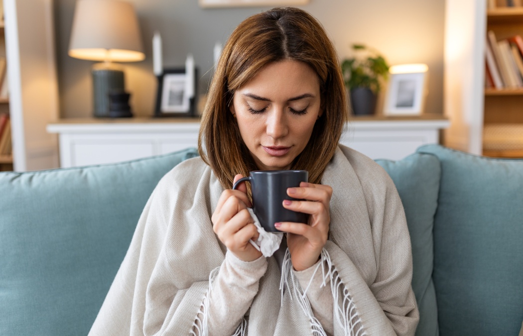 Sickness, seasonal virus problem concept. Woman being sick having flu drinking tea on sofa. Sick woman lying in bed with high fever. Cold flu and migraine.