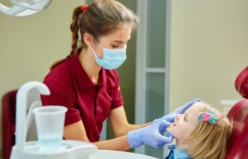 Pediatric dentist examining little girls teeth in the dentists chair at the dental clinic